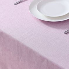 a white plate on top of a pink table cloth with silverware next to it