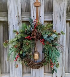 a wreath hanging on the side of a wooden door with a bell and evergreens