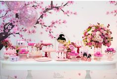 a table topped with lots of pink flowers and cake next to a wall covered in balloons