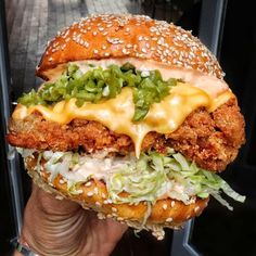 a chicken sandwich with cheese, lettuce and mayonnaise is held in front of some plants