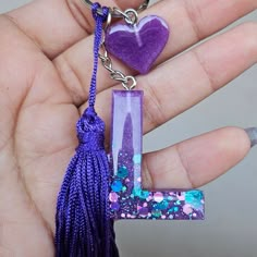 a hand holding a purple letter shaped keychain with a heart hanging from it