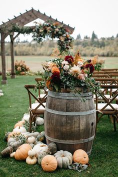 a wooden barrel with flowers and pumpkins on the grass in front of an outdoor ceremony