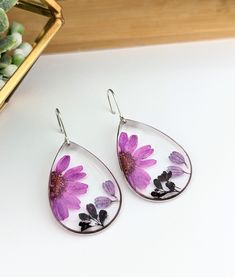 purple flowers painted on tear shaped glass dangles are displayed in front of a potted plant