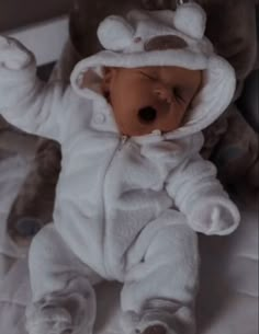 a baby in a white bear suit laying on top of a bed