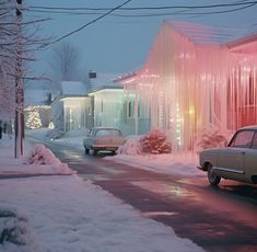 two cars parked on the side of a road covered in snow next to buildings and trees