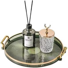 a glass tray with a bottle and candle on it next to a gold plated container