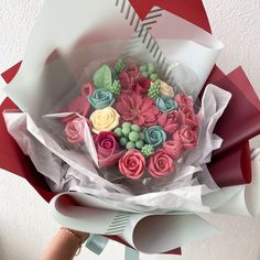 a person holding a bouquet of flowers made out of fondant icing and paper