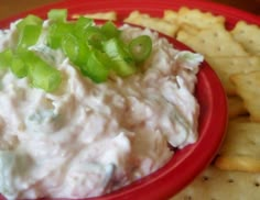 a red bowl filled with dip and crackers on top of a table next to chips