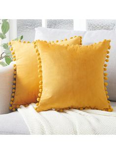 two yellow pillows with pom - poms on them sitting on a white couch