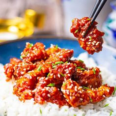 someone is holding chopsticks over some food on top of white rice in a blue bowl