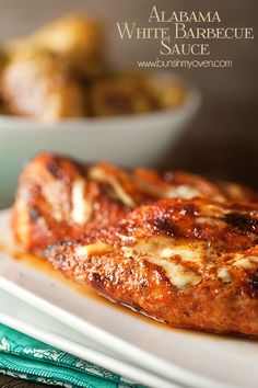 a white plate topped with meat covered in sauce on top of a table next to other food