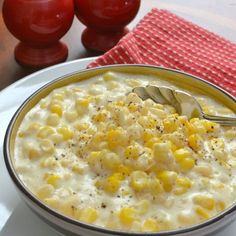 a bowl filled with corn on top of a white plate next to two red tomatoes