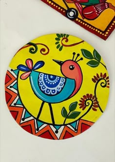 two colorful painted plates sitting next to each other on a white counter top, one has a bird and the other has flowers