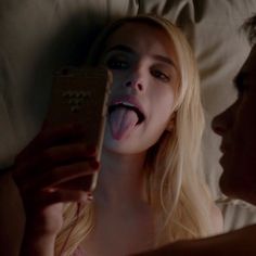 a woman laying in bed with her mouth open and tongue out while holding a cell phone