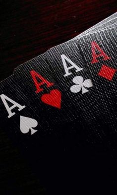 playing cards with ace symbols on them sitting on a wooden table in front of a black background