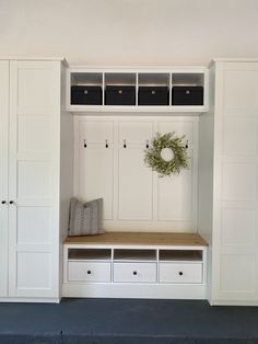 an entryway with white cabinets, drawers and a wreath hanging on the coat rack