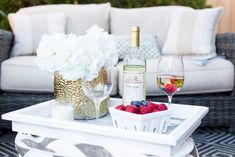 a glass of wine and some berries on a tray near a bottle of white wine