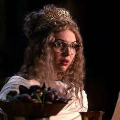 a woman wearing glasses and a tiara sitting in front of a bowl of fruit