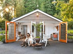 a woman sitting on a chair in front of a shed with orange trimmings