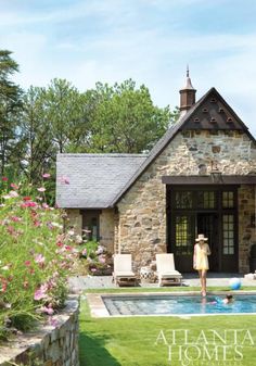 a woman standing in front of a pool next to a stone building with a swimming pool