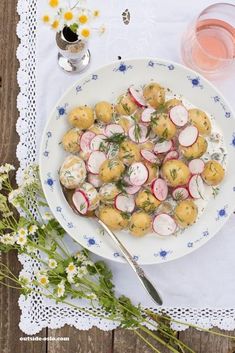 a white plate topped with radishes next to a glass of water and flowers