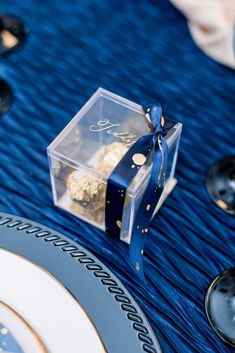 a blue table cloth with plates, silverware and a clear box containing gold decorations