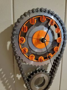 an orange and black clock on the wall with chains attached to it's sides