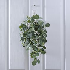 a wreath hanging on the front door with white flowers and greenery around it's edges