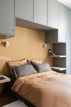 a bed sitting in a bedroom next to a wall mounted book shelf and cupboards