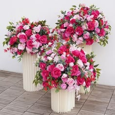 three white vases filled with pink and red flowers on top of a wooden floor