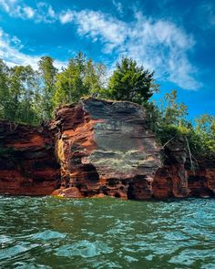 a large rock formation in the middle of a body of water with trees around it