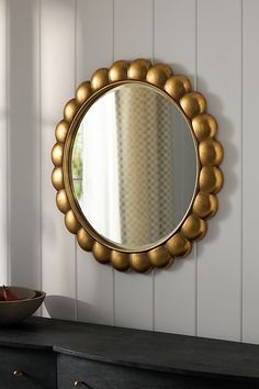 a round mirror hanging on the wall above a black dresser and bowl with apples in it