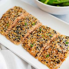 two pieces of salmon with sesame seeds on a white plate next to a bowl of broccoli