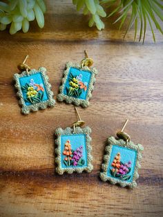 three small pictures hanging from hooks on a wooden table next to a potted plant