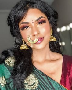 a woman with long black hair wearing a green and gold saree, nose ring and earrings