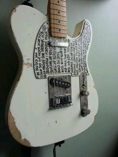 an old white guitar is hanging on the wall in front of a green wall with writing all over it