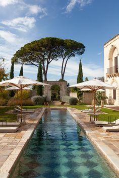 an outdoor swimming pool surrounded by lawn chairs and umbrellas with trees in the background