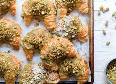 several pastries on a baking sheet with pistachio toppings and a bowl of pistachio