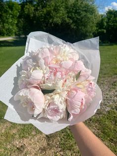 a bouquet of pink and white flowers is held in someone's hand on the grass