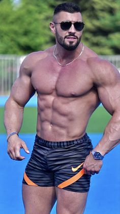 a shirtless man in black shorts and sunglasses standing on a blue surface with an orange ring around his neck