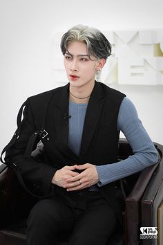 a person sitting in a chair wearing a black suit and blue shirt with silver hair