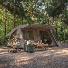 a tent set up in the middle of a forest with picnic tables and chairs around it