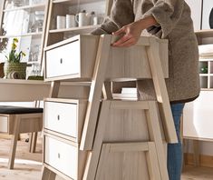 a woman standing on top of a wooden ladder next to a shelf filled with drawers