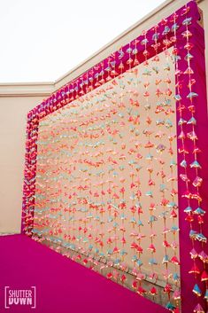 an art installation made out of pink fabric and colorful beads on the side of a building