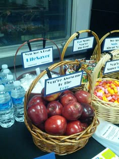 two wicker baskets filled with apples next to water bottles and candy bar signs on a table