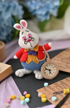 a crocheted rabbit holding a clock on top of a table