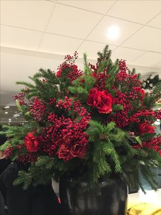 red flowers and greenery in a black vase on a counter top at a store