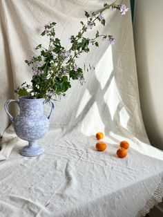 a vase filled with flowers sitting on top of a table next to three oranges