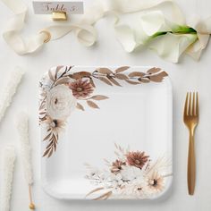 a white plate with flowers on it next to gold utensils