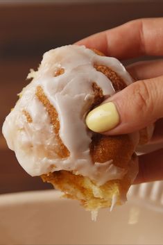 a person holding a doughnut with icing on it in front of a bowl